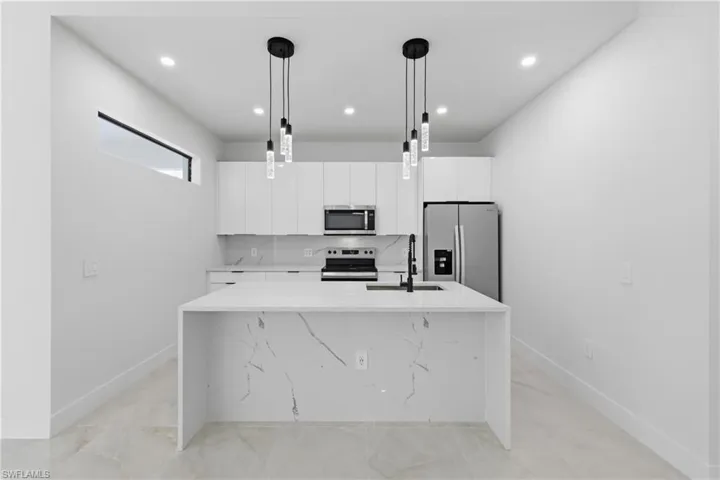 Kitchen featuring white cabinetry, light stone countertops, stainless steel appliances, a kitchen island with sink, and hanging light fixtures