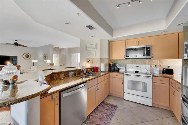Kitchen featuring ceiling fan, tasteful backsplash, stainless steel appliances, a raised ceiling, and track lighting
