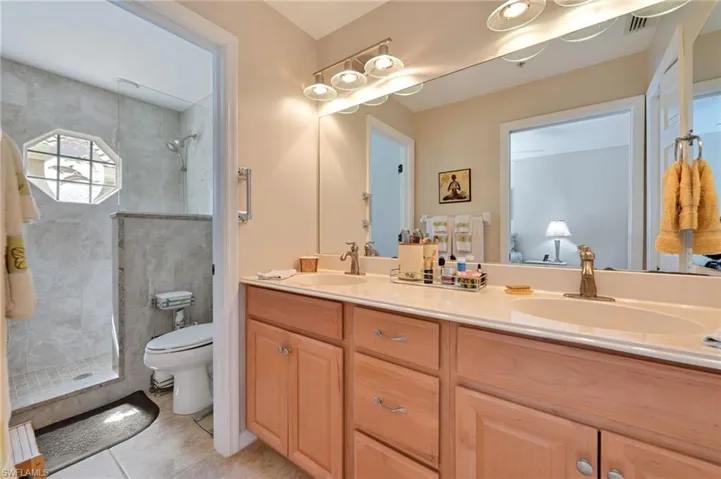 Bathroom with tile floors, a tile shower, double vanity, and toilet