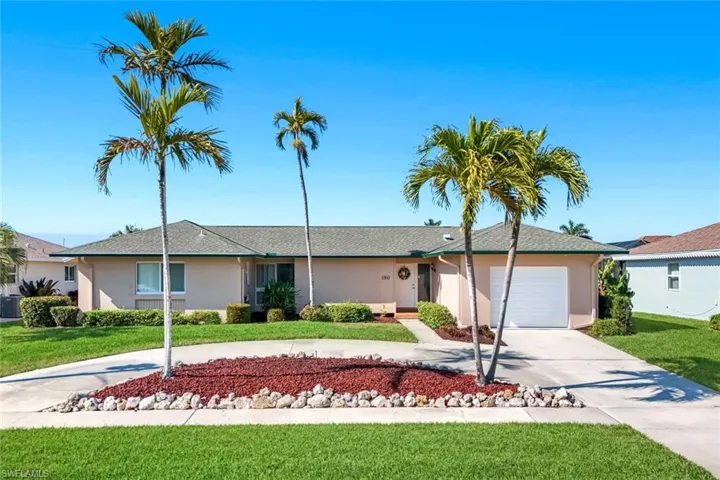 Ranch-style home with curved driveway, a front lawn, an attached garage, and stucco siding