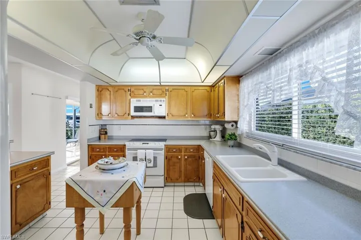 Kitchen with white appliances, a ceiling fan, light countertops, decorative backsplash, and wood finish cabinetry