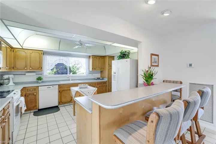 Kitchen featuring light countertops, white appliances, a breakfast bar, light tile patterned floors, and wood finish cabinetry