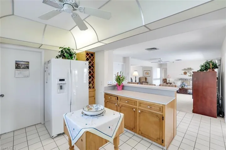 Kitchen with a ceiling fan, white refrigerator with ice dispenser, light countertops, open floor plan, and a peninsula
