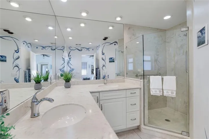Full bath with double vanity, a marble finish shower, recessed lighting, and light tile patterned floors