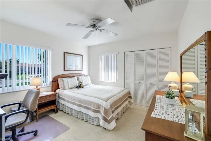 Carpeted bedroom with an office area, multiple windows, and a ceiling fan