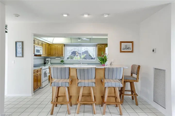Kitchen featuring light countertops, a breakfast bar area, a peninsula, white appliances, and wood finish cabinets