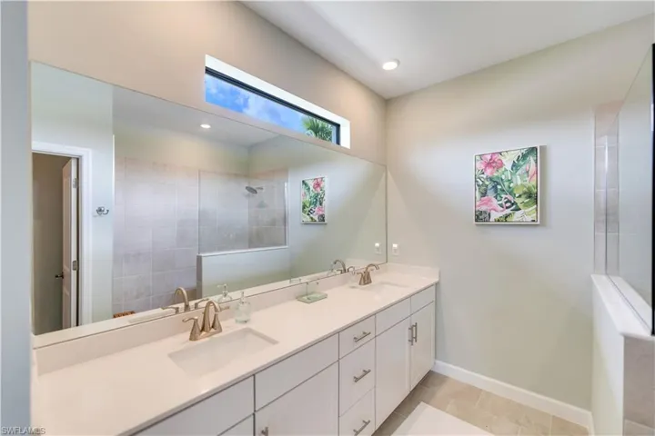 Bathroom with tile patterned flooring, tiled shower, and dual bowl vanity