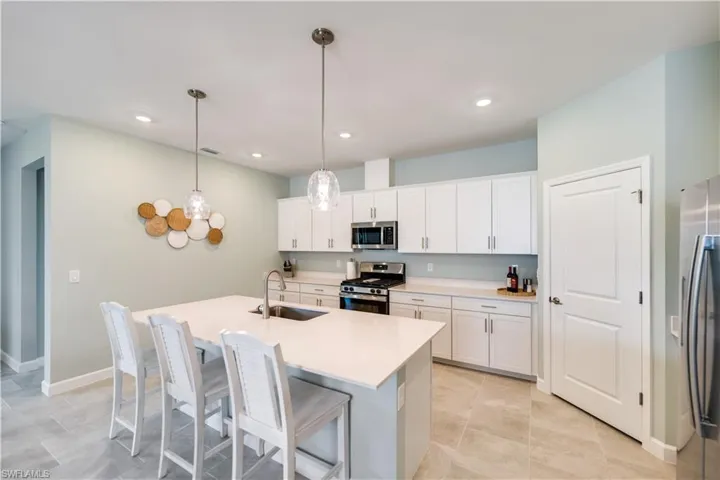 Kitchen featuring stainless steel appliances, white cabinets, sink, hanging light fixtures, and an island with sink