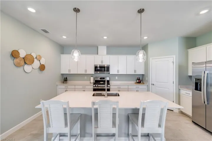 Kitchen featuring light tile patterned flooring, appliances with stainless steel finishes, decorative light fixtures, and white cabinetry