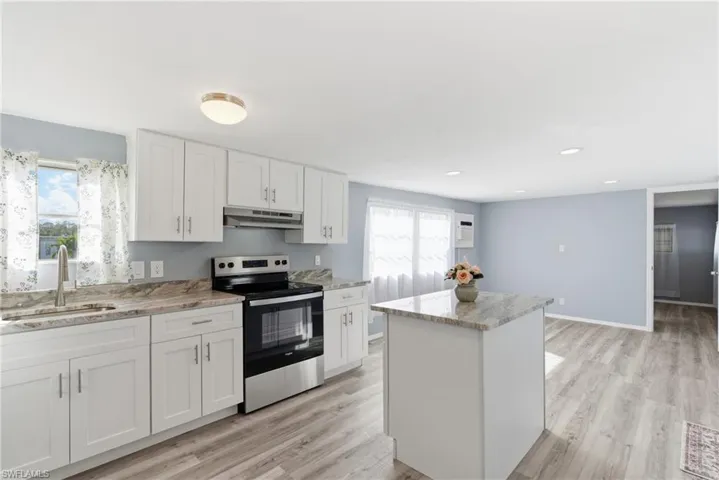 Kitchen with stainless steel electric range oven, white cabinetry, a kitchen island, and healthy amount of natural light