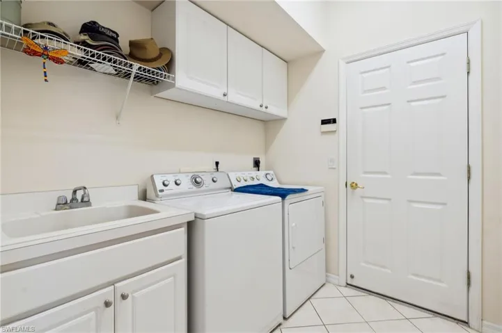 Laundry area featuring separate washer and dryer, cabinets, sink, and light tile patterned flooring