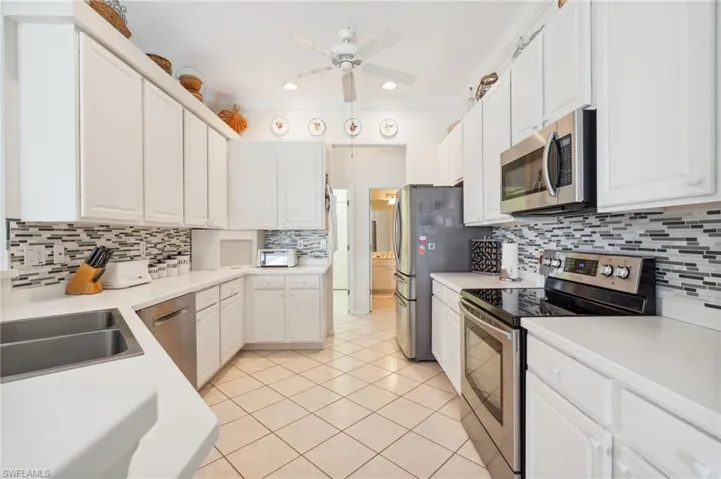 Kitchen with white cabinetry, light tile patterned floors, ceiling fan, decorative backsplash, and appliances with stainless steel finishes