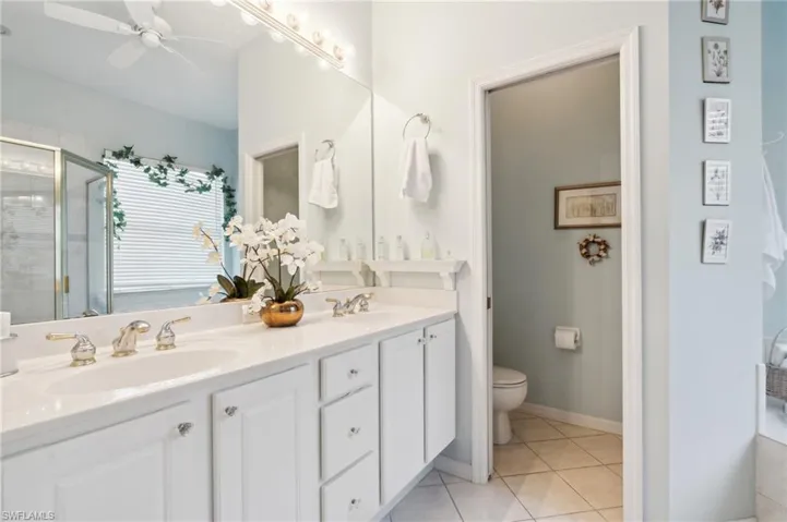 Bathroom with toilet, tile patterned floors, vanity, ceiling fan, and a shower with shower door