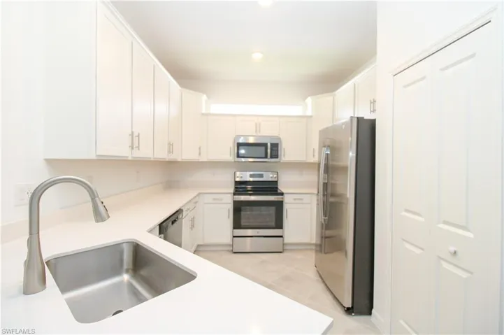 Kitchen featuring sink, light tile patterned flooring, white cabinets, and stainless steel appliances