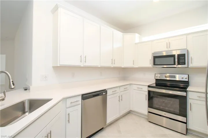 Kitchen featuring light tile patterned flooring, appliances with stainless steel finishes, sink, and white cabinets