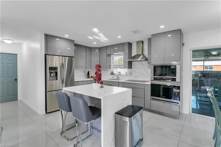 Kitchen with gray cabinetry, appliances with stainless steel finishes, a sink, modern cabinets, and wall chimney exhaust hood
