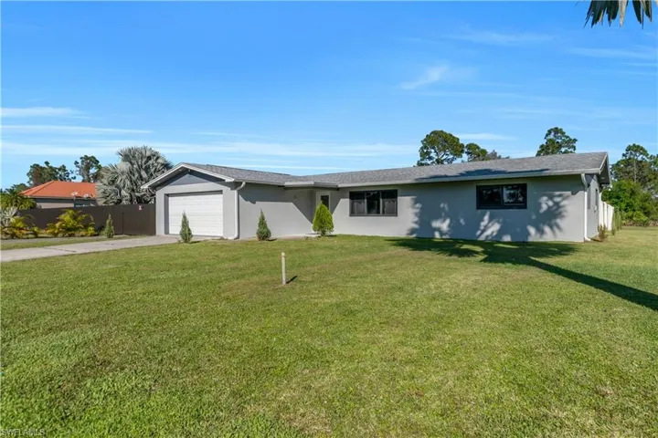 Ranch-style home with a garage, driveway, a front lawn, and stucco siding
