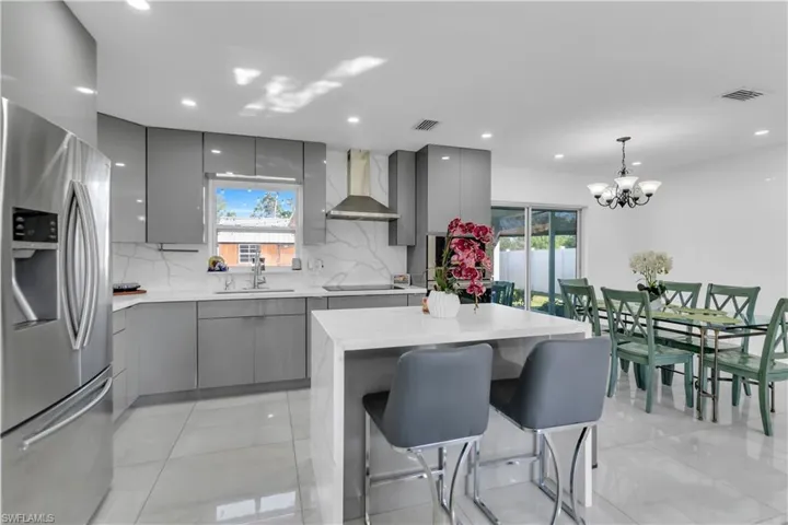Kitchen with stainless steel refrigerator with ice dispenser, black electric stovetop, gray cabinets, wall chimney range hood, and modern cabinets