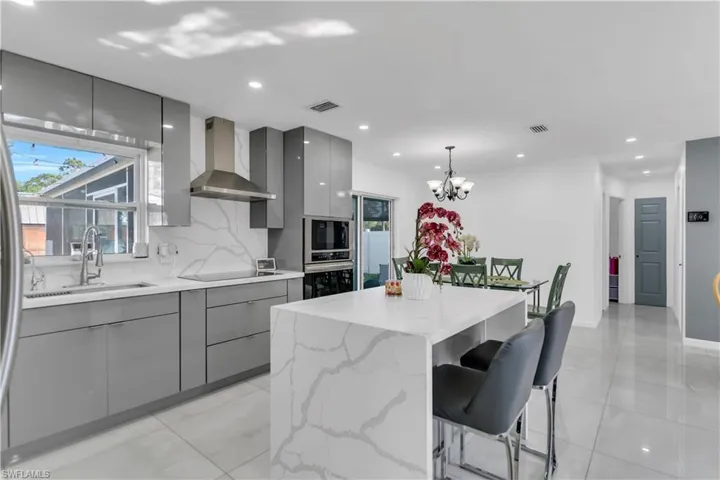 Kitchen with wall chimney exhaust hood, modern cabinets, a sink, and gray cabinetry