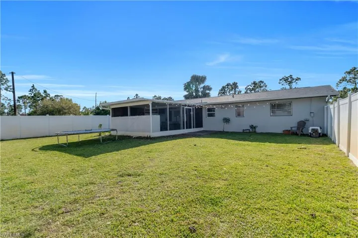 Back of house featuring a sunroom, a fenced backyard, a trampoline, and a yard