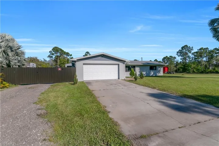 View of front of house featuring stucco siding, an attached garage, a gate, driveway, and a front lawn