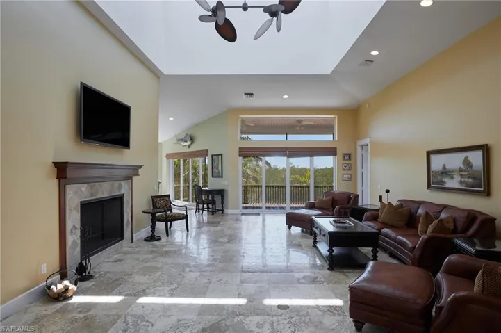 Living area with fireplace, soaring ceiling, looking toward the large screened-in balcony, which looks out over the firepit area and boat dock