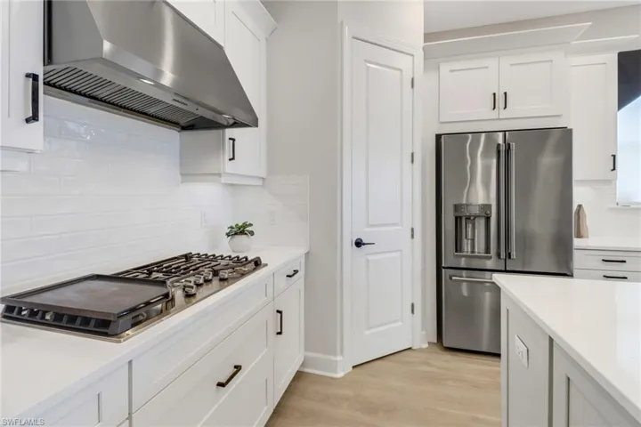 Kitchen featuring stainless steel appliances, white cabinets, extractor fan, and light hardwood / wood-style floors