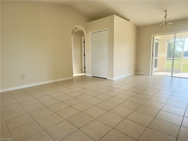 Tiled empty room featuring a notable chandelier and vaulted ceiling
