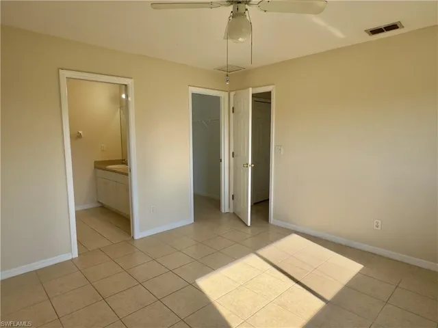 Unfurnished bedroom featuring ceiling fan, a closet, ensuite bath, light tile floors, and a walk in closet