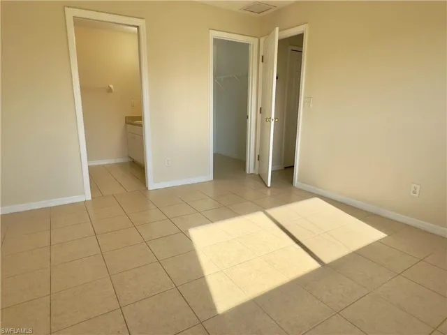 Unfurnished bedroom featuring a walk in closet, a closet, ensuite bathroom, and light tile floors