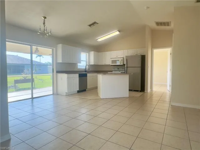 Kitchen with light tile floors, white cabinetry, vaulted ceiling, and stainless steel appliances