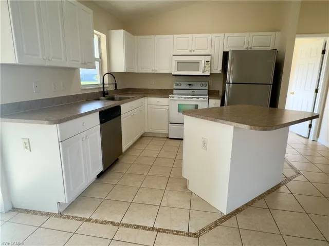 Kitchen featuring white cabinetry, sink, light tile floors, and stainless steel appliances