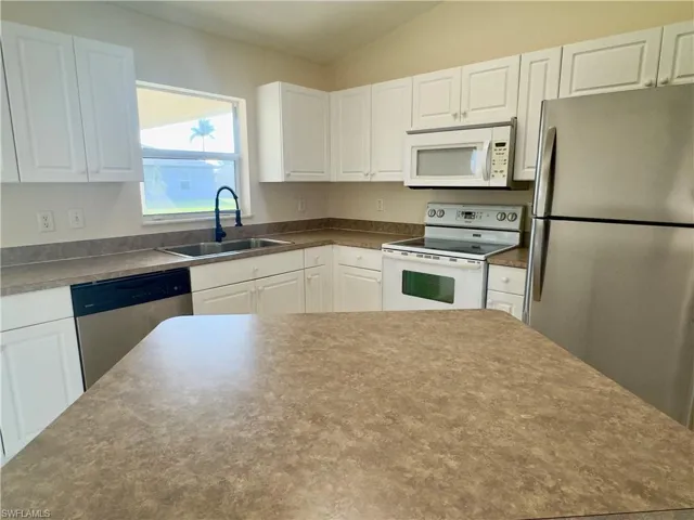 Kitchen with sink, stainless steel appliances, lofted ceiling, and white cabinetry