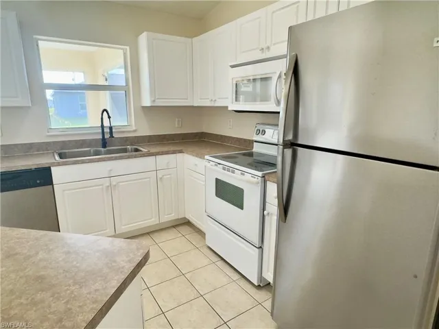 Kitchen with white cabinets, appliances with stainless steel finishes, sink, and light tile floors