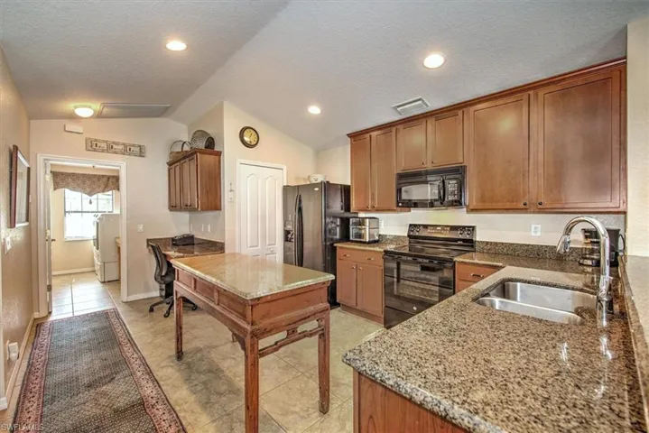 Kitchen with washer / dryer, sink, stone countertops, vaulted ceiling, and black appliances