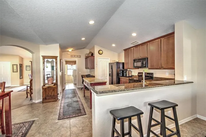 Kitchen with a breakfast bar area, vaulted ceiling, kitchen peninsula, dark stone counters, and black appliances