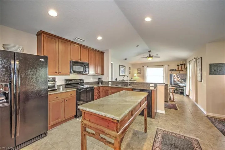 Kitchen featuring sink, ceiling fan, black appliances, vaulted ceiling, and kitchen peninsula