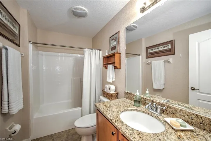 Full bathroom with vanity, shower / bath combination with curtain, a textured ceiling, and toilet