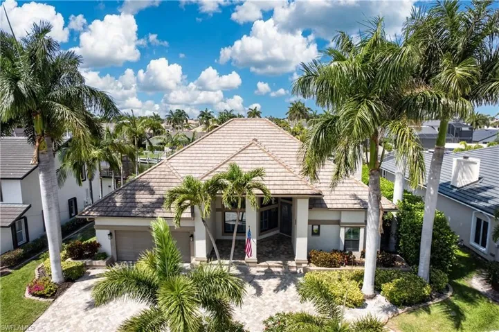 The property features a tiled roof, a paved driveway, and lush landscaping with mature palm trees