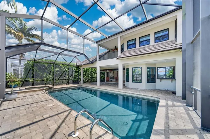 The property features a screened-in swimming pool area with a paver patio, surrounded by lush green foliage