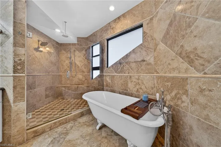 Bathroom featuring a freestanding clawfoot bathtub, a walk-in shower with a glass enclosure, and stone tile walls and flooring