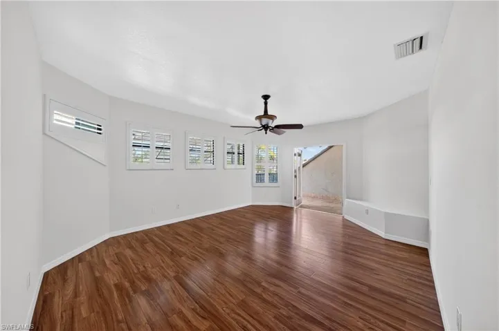 Spacious living area featuring rich wood flooring, white walls, and a ceiling fan
