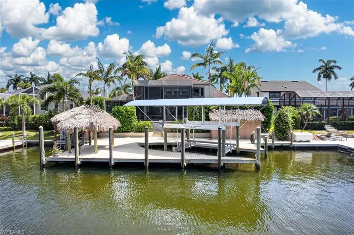 The property features a private dock with a covered boat lift, a thatched-roof tiki hut, and direct water access