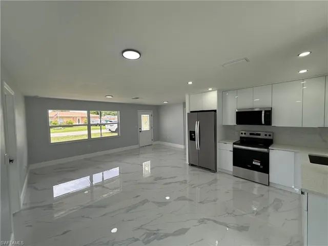 Kitchen featuring appliances with stainless steel finishes, modern cabinets, light marble finish floors, white cabinetry, and open floor plan