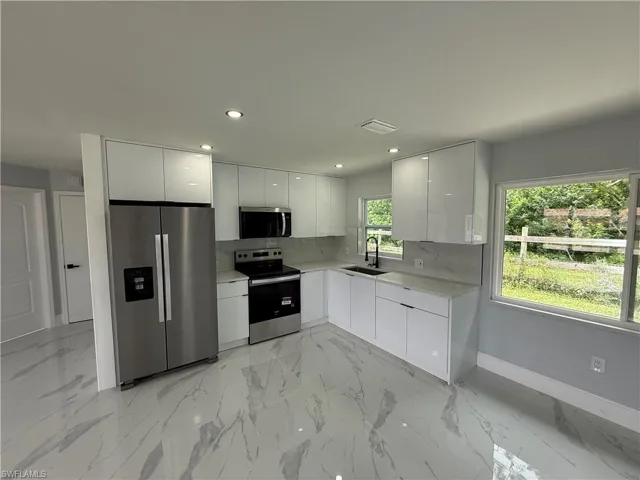 Kitchen featuring modern cabinets, stainless steel appliances, light marble finish flooring, white cabinets, and light countertops