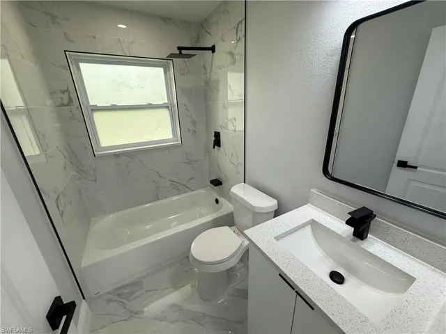 Full bathroom with vanity, tub / shower combination, marble look tiles, and a textured wall