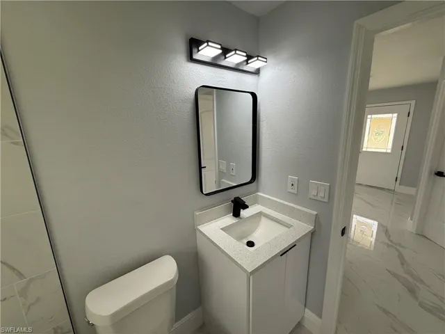 Bathroom with marble finish flooring, vanity, and a textured wall