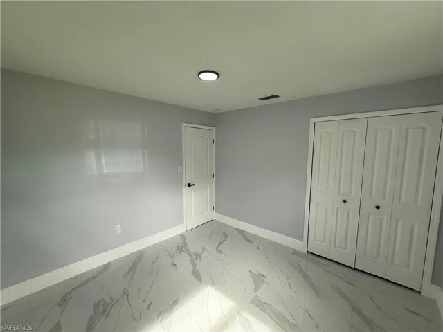 Unfurnished bedroom with marble finish floors and a closet