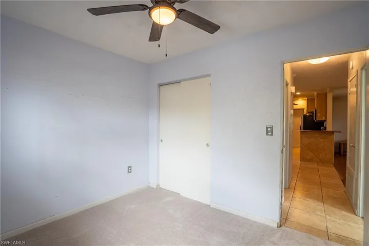 Unfurnished bedroom with a closet, light tile flooring, ceiling fan, and fridge