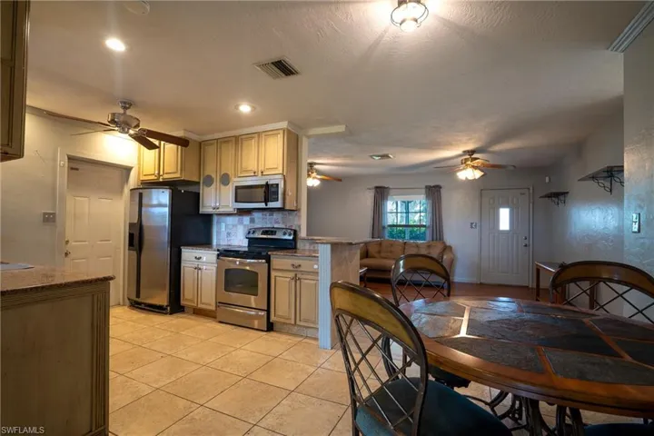 Kitchen featuring light brown cabinets, light tile flooring, stainless steel appliances, backsplash, and ceiling fan